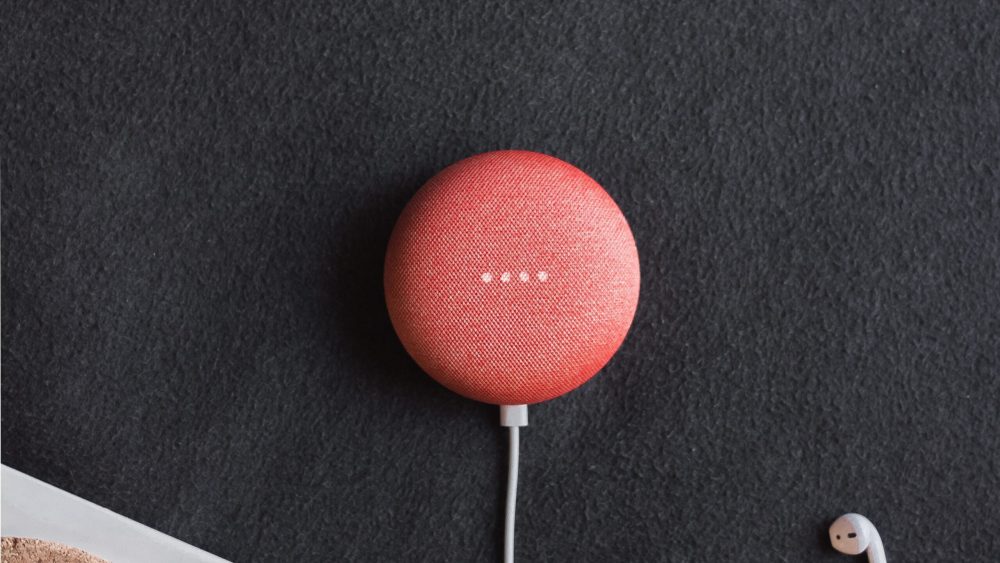 flat lay photography of coral Google Home Mini on black surface beside Apple AirPods