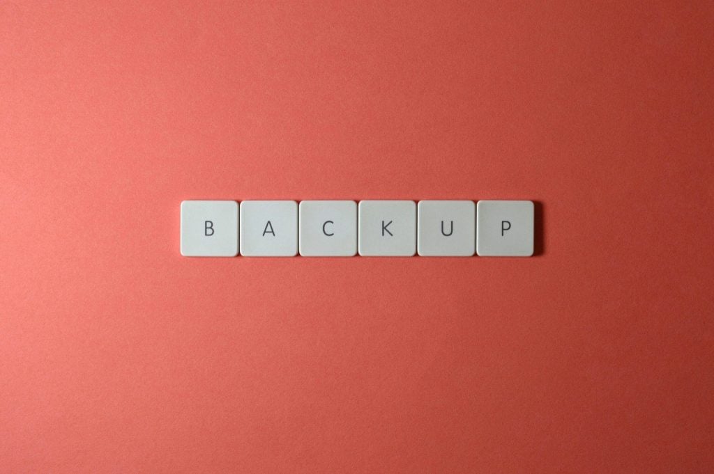 Free Close-up of keyboard keys spelling 'BACKUP' placed on a coral-colored surface. Stock Photo