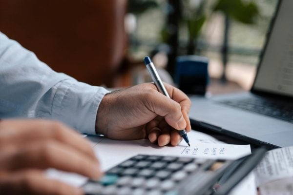 Free A person calculating finances with a calculator and pen on a desk indoors. Stock Photo