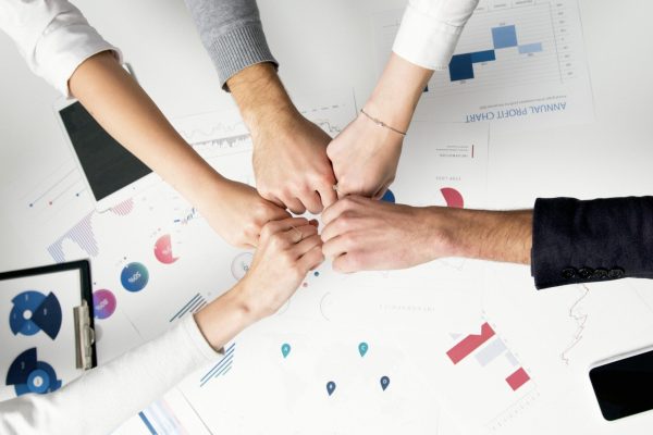 Free Colleagues celebrate success with a fist bump over financial charts depicting teamwork and unity. Stock Photo