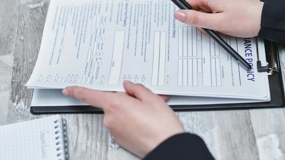 Free Close-up of hands analyzing insurance policy paperwork with pen on table. Stock Photo